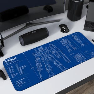 Può includere: Un tappetino da scrivania rettangolare blu con un disegno di progetto di un robot Gundam. Il tappetino include specifiche tecniche e diagrammi in bianco. Altri oggetti sulla scrivania includono un altoparlante nero, cuffie, un mouse e un controller di gioco.