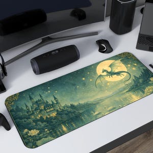 Puede incluir: Alfombrilla de escritorio rectangular con un paisaje de fantasía que representa un castillo, un lago y un dragón volando frente a una luna llena. La alfombrilla tiene un borde dorado. Otros accesorios de escritorio.