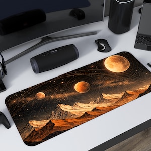 Op de afbeelding: Een rechthoekige bureaumat met een ruimtethema-ontwerp met planeten, bergen en een sterrenhemel in oranje, bruin en zwart. Omringd door zwarte technische accessoires, waaronder een monitor, luidsprekers en een gamecontroller.