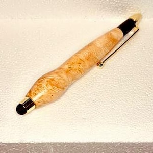 May include: A handcrafted pen with a light brown, wood-grain barrel. The pen features gold-colored accents, a black tip, and a gold-colored clip. The pen is designed for use with touchscreens and is a stylish writing accessory.