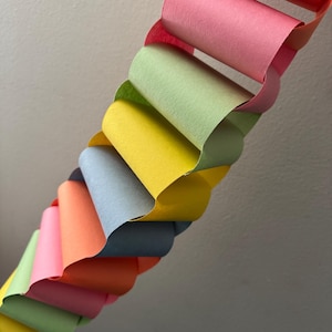 May include: A colorful paper chain garland in a variety of pastel colors, including pink, green, yellow, and blue. The chain is made of looped paper strips, creating a decorative and festive look. Perfect for party decorations or craft projects.