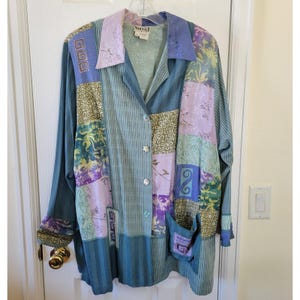 Puede incluir: Chaqueta patchwork de manga larga en tonos verde azulado, lavanda y verde oliva. La chaqueta presenta un cuello, cierre de botones y dos bolsillos delanteros. La tela es una mezcla de paneles estampados y lisos.