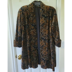 Könnte beinhalten: Ein langer Mantel mit floralem Muster in Braun, Gold und Schwarz hängt an einer Tür. Der Mantel hat eine samtige Textur und ein dunkelgraues Futter. Die Ärmel sind umgeschlagen und der Mantel ist vorne offen.