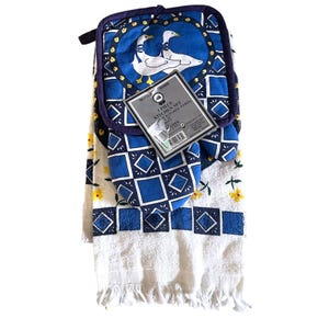 May include: A three-piece kitchen set featuring a white towel with yellow flower embroidery and blue diamond borders, a blue oven mitt, and a blue pot holder with a white goose graphic. The set includes a product tag labeled Better Home.