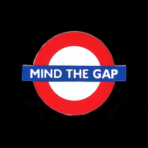 May include: A round, red and white graphic with a blue rectangular banner. The text "MIND THE GAP" is displayed in white letters on the blue banner. The graphic is set against a black background.
