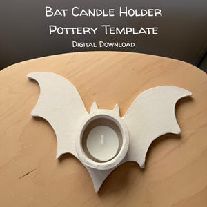 May include: A white, bat-shaped pottery candle holder with a circular center opening containing a small white tea light candle. The text above reads: BAT CANDLE HOLDER POTTERY TEMPLATE DIGITAL DOWNLOAD.