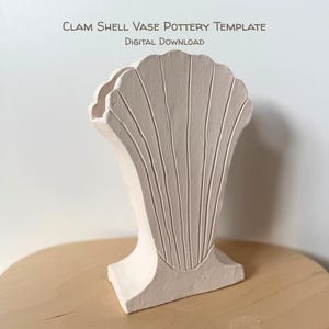 Op de afbeelding: Een lichtbeige clamshell vaas pottenbak sjabloon. De vaas heeft een clamshell ontwerp met verticale lijnen en de tekst "CLAM SHELL VASE POTTERY TEMPLATE DIGITAL DOWNLOAD". De vaas staat op een lichtbruin oppervlak.