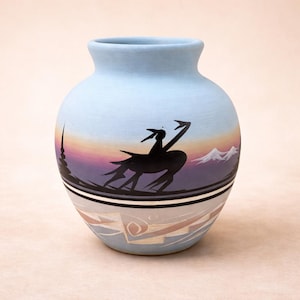 May include: A light blue ceramic vase with a rounded body and a narrow neck. The vase features a painted landscape scene with a black silhouette figure, mountains, and a sunset. The bottom has geometric patterns.