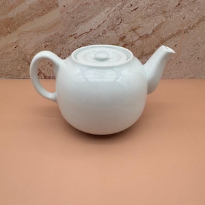 May include: A white ceramic mug with a black handle and the text "But First, Coffee" in a bold, black font. The mug is set against a blurred background, suggesting a cozy setting.