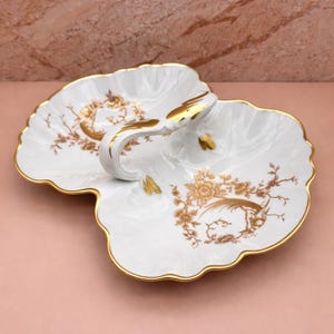 May include: White porcelain serving dish with a gold handle and rim. The dish features a floral and bird design in gold. The scalloped edges add a decorative touch to this elegant serving piece.