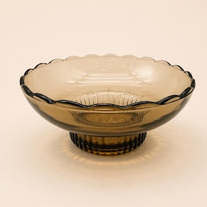 May include: A vintage amber-colored glass bowl with a scalloped rim and a pedestal base. The bowl has a decorative design and is likely used for serving or display. The glass has a glossy finish.