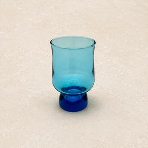 May include: A small, turquoise-colored glass with a rounded top and a dark blue base. The glass has a simple, elegant design and is likely used for serving beverages. The glass is approximately 3 inches tall.