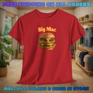May include: Red t-shirt with a Big Mac graphic. The burger illustration shows two beef patties, cheese, lettuce, and sauce. The text "Big Mac" is above the burger. The shirt also has the text "FREE SHIPPING ON ALL ORDERS" and "MULTIPLE COLOURS & SIZES IN STOCK".