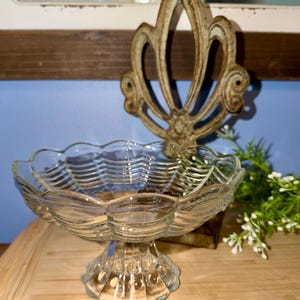May include: A clear glass pedestal bowl featuring a scalloped rim and a textured basket-weave pattern on the exterior. The bowl stands on a short, thick base with vertical ribbing and a circular foot, showcasing a transparent and reflective surface.