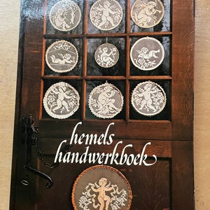 May include: A book titled "Hemels handwerkboek" by Marie van den Berk-Mertens. The cover features a wooden door with nine framed images of crocheted angels. The book is published by Cantecleer.