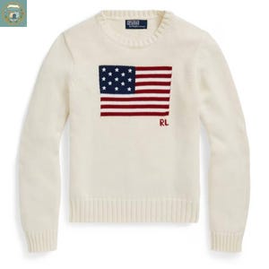 May include: Cream-colored sweater featuring a knitted American flag design on the front. The flag has a blue field with white stars and red and white stripes. The letters "RL" are embroidered in red below the flag.