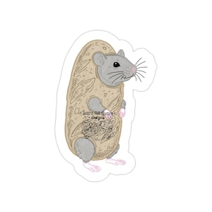 May include: A sticker showing a grey rat in a tan baguette costume. The baguette has a detailed design and the text "here me there + designs". The rat has pink paws and whiskers.