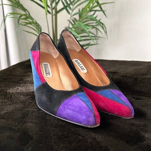 May include: A pair of black suede heels with purple, blue and pink accents. The heels have a pointed toe and the brand name "BALLY" is written on the inside of each shoe.