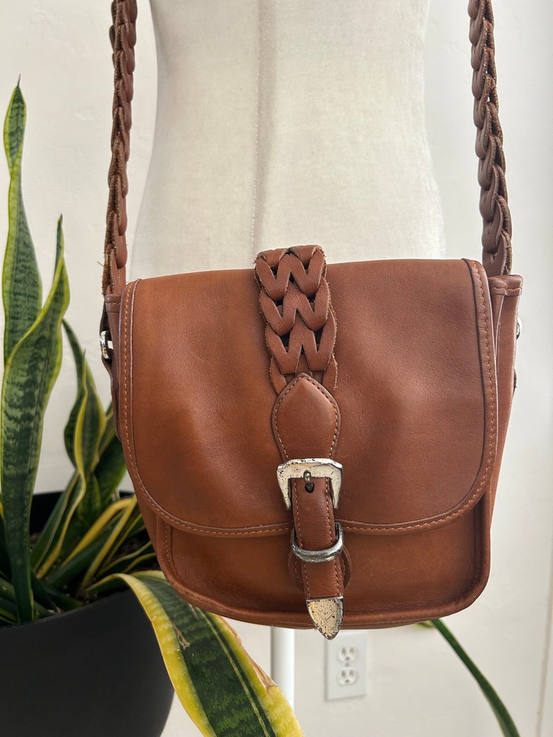 May include: A brown leather crossbody bag with a braided strap and a silver buckle.