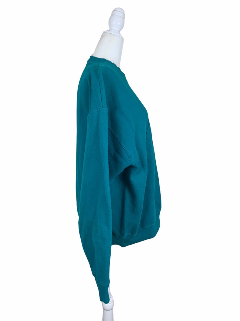 May include: Teal blue sweatshirt with a crew neck and long sleeves.