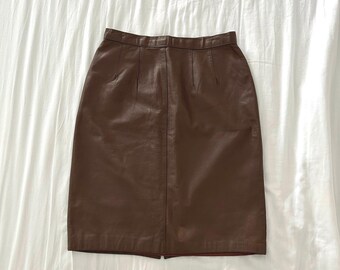 May include: A brown leather skirt with a straight cut and a zipper closure. The skirt is knee-length and has a simple design.