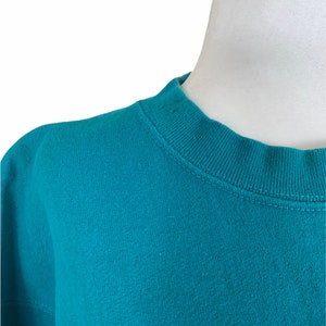 May include: Close-up of a teal blue sweatshirt with a ribbed crew neck.