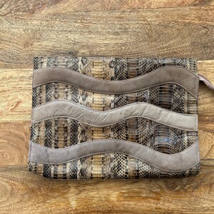 Könnte beinhalten: Eine braune und beige Schlangenleder-Clutch mit einem wellenförmigen Wildleder-Design. Die Clutch hat einen Reißverschluss und einen braunen Schlangenleder-Riemen.
