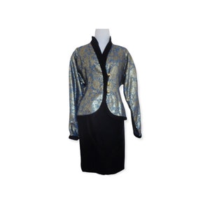 Puede incluir: Un traje de dos piezas con una chaqueta estampada en dorado y azul y una falda negra.