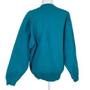 May include: Teal blue sweatshirt with long sleeves and a crew neck.