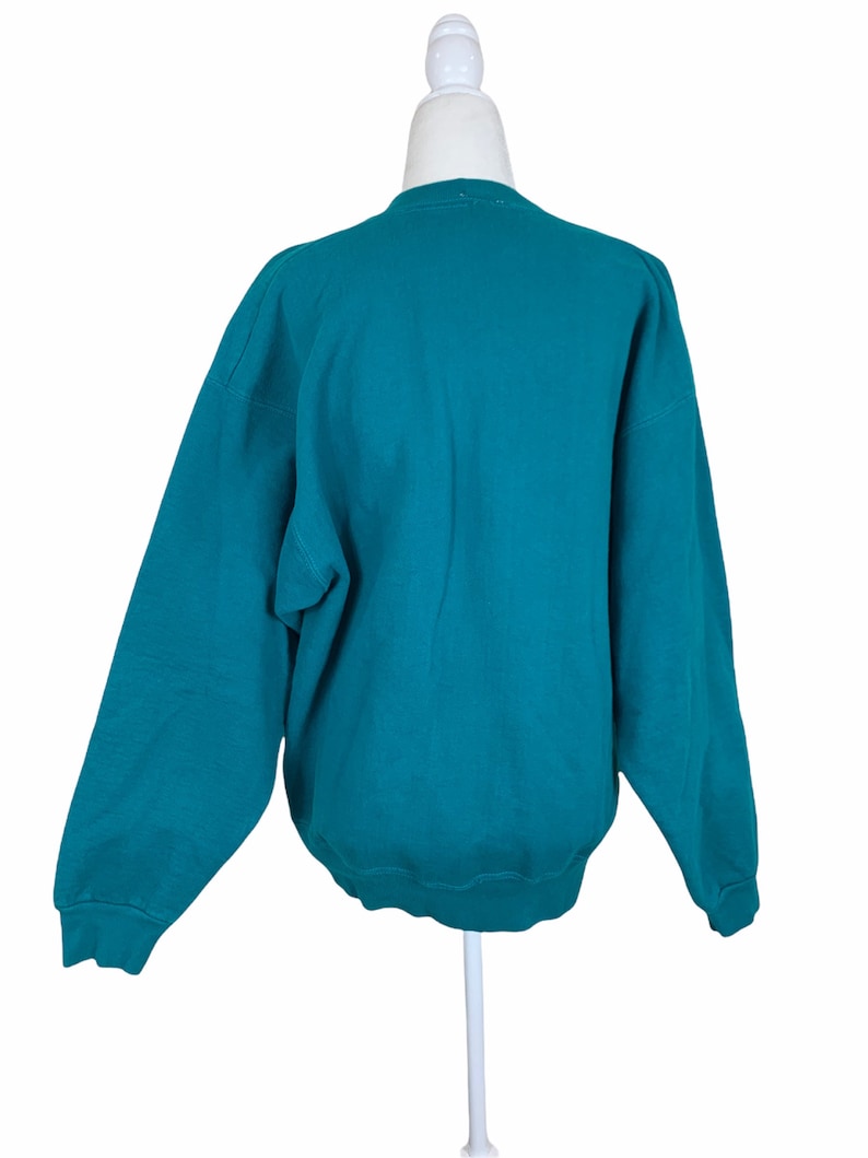 May include: Teal blue sweatshirt with long sleeves and a crew neck.