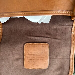 May include: A brown leather bag with a brown canvas lining. The bag has a label that reads "The Gibson Collection Brighton" and includes a description of the leather.