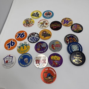 May include: A collection of vintage pogs featuring various designs and logos. The pogs include images from Universal Studios, McDonald's, and other brands. The colors are vibrant, with a mix of circular and octagonal shapes.