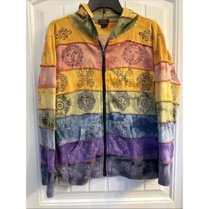 May include: A colorful zip-up hoodie with a patchwork design. The jacket features a rainbow of colors, including yellow, orange, green, blue, and purple. Each panel is adorned with sun and floral patterns. The hoodie has a hood and two front pockets.