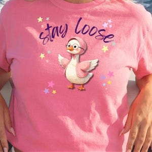 A person wearing a pink t-shirt with a cartoon duck and the text "Stay loose" printed on it.