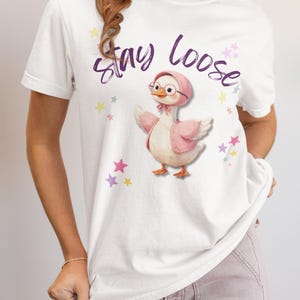 A woman wearing a white t-shirt with a cartoon duck and the text "Stay Loose" printed on it.