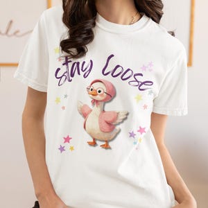 A woman wearing a white t-shirt with a cartoon image of a duck and the text "Stay Loose" printed on it.
