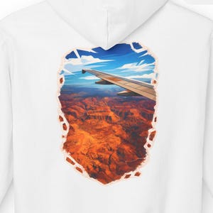 May include: White hoodie featuring a scenic view of a canyon and airplane wing, framed within a torn-paper effect. The back of the hoodie displays a colorful landscape of red rock formations under a blue sky. A small patch on the upper right reads "WINDOW SEAT CLUB".