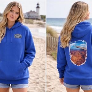 May include: A royal blue hoodie with a front pocket and a hood. The front of the hoodie has a small patch that says "Window Seat Club". The back of the hoodie has a graphic of an airplane wing over a canyon.