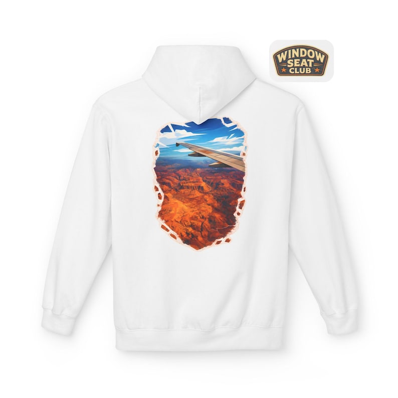 May include: White hoodie featuring a scenic view of a canyon and airplane wing, framed within a torn-paper effect. The back of the hoodie displays a colorful landscape of red rock formations under a blue sky. A small patch on the upper right reads "WINDOW SEAT CLUB".