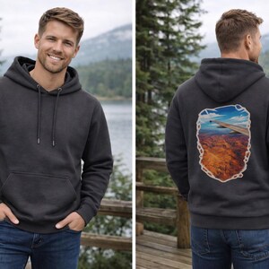 May include: Charcoal gray hoodie with a front pocket and drawstring hood. The back of the hoodie features a colorful graphic of a landscape scene. The model is wearing blue jeans.
