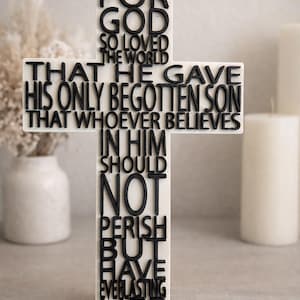 May include: A white cross with black raised lettering. The text reads "For God so loved the world that He gave His only begotten Son that whoever believes in Him should not perish but have everlasting life."