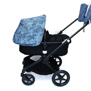 May include: A black stroller with a blue floral patterned canopy and matching handlebar mitts. The stroller has four black wheels and a black frame. The canopy and mitts have a blue floral design.