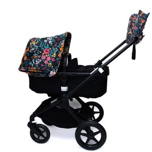 Könnte beinhalten: Schwarzer Kinderwagen mit floral bedrucktem Verdeck und Griffbezügen. Das Blumenmuster umfasst rosa, gelbe und blaue Blumen auf dunklem Hintergrund. Der Kinderwagen hat vier schwarze Räder und einen schwarzen Rahmen.