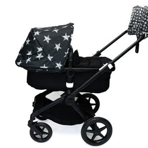 May include: A black stroller with a canopy and handle covers featuring a white star pattern. The stroller has a black frame, wheels, and a bassinet-style seat. The wheels are approximately 10 inches in diameter.