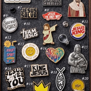 May include: A collection of enamel pins with religious themes. Designs include the word "Jesus" in various fonts, a heart, a crown, a smiley face, and images of Jesus. The pins are in various colors and shapes.