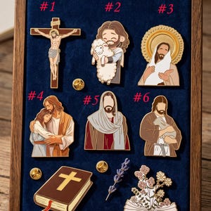 May include: A collection of eight religious enamel pins displayed in a wooden frame with a blue velvet backing. The pins depict various religious figures and symbols, including Jesus, a cross, and a Bible.