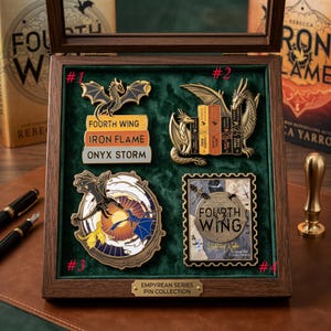 May include: A wooden display case with four dragon-themed pins from the "Empyrean Series Pin Collection." The pins feature dragons, book stacks with titles like "Fourth Wing," and a stamp design. The case has a green velvet interior.