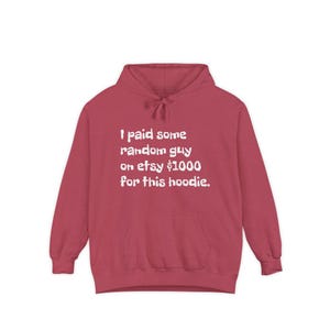 May include: A maroon hoodie with a front pocket and a drawstring hood. The white text on the front reads: "I paid some random guy on etsy $1000 for this hoodie."