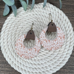 May include: A pair of dangle earrings with a brown leather accent and a white and peach floral pattern.