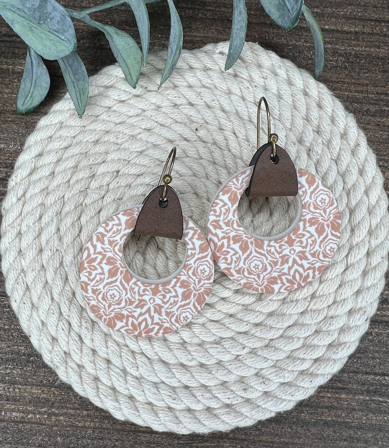 May include: A pair of dangle earrings with a brown leather accent and a white and peach floral pattern.